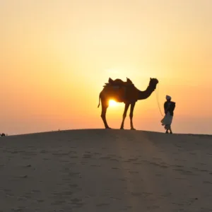 Individual leading a camel through the desert, illustrating the need for medical emergency flights from remote and deserted locations.